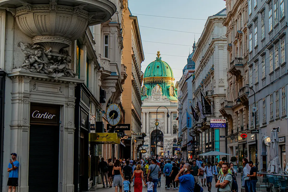 Centre de Vienne, en Autriche. Rue commerçante animée et achalandée avec la boutique Cartier au premier plan et un un bâtiment historique au bout de la rue.