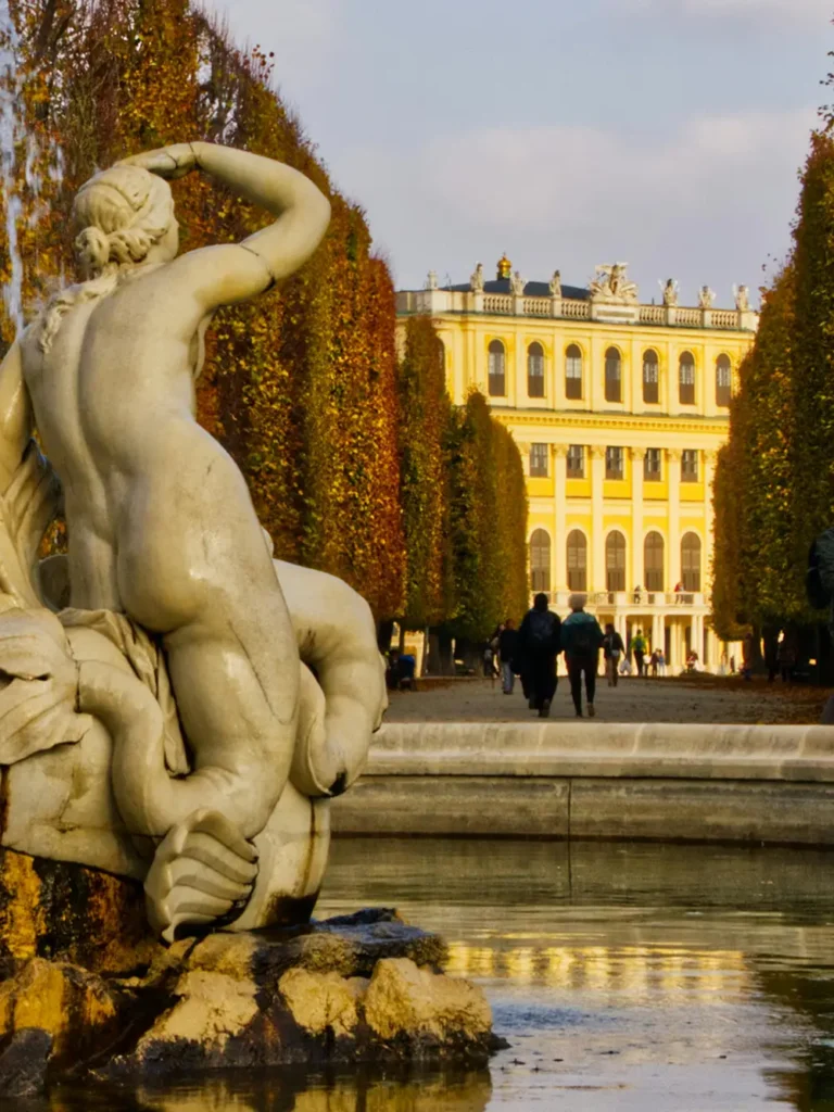 Statue de fontaine au premier plan et vue automnale sur le château de Schönbrunn et ses jardins à Vienne.