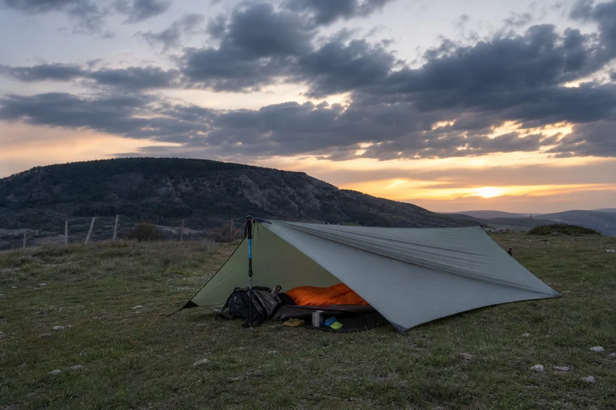 Tarp de bivouac ultralight pour trek longue durée Tarp de bivouac ultralight tendu avec des bâtons de randonnée sur un terrain herbeux en montagne