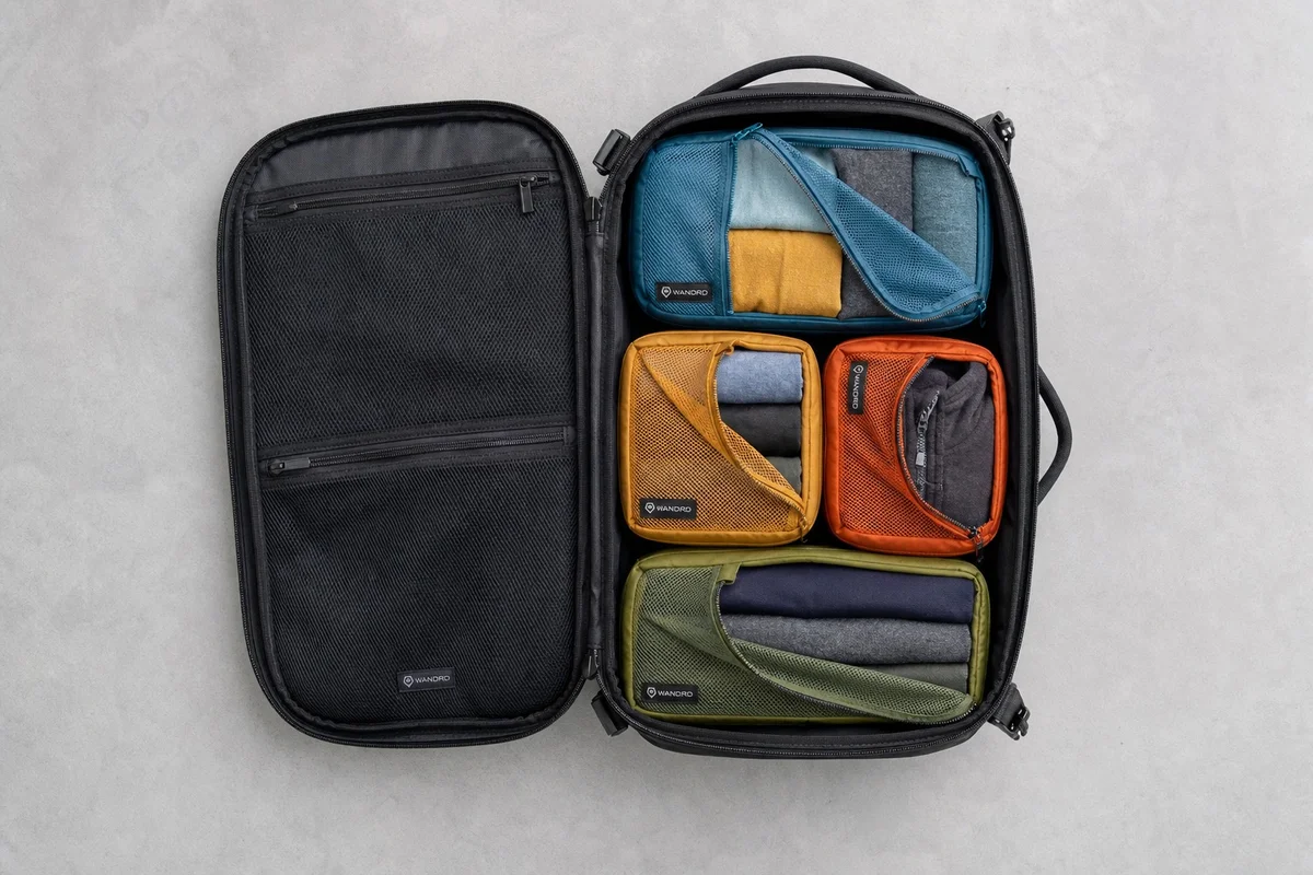 Sélection de vêtements techniques de voyage en laine mérinos pliés dans des cubes de rangement colorés dans un sac à dos